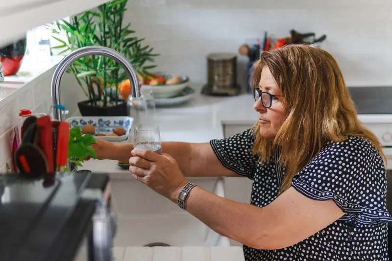 Woman filling a glass with water at a kitchen tap